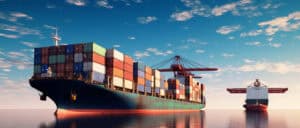 Large container cargo ships loaded with colorful shipping containers sailing on calm ocean waters under a clear blue sky with scattered clouds