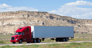 Semi-truck with a red cab and gray trailer driving through a desert landscape, representing logistics and freight transportation services in China.
