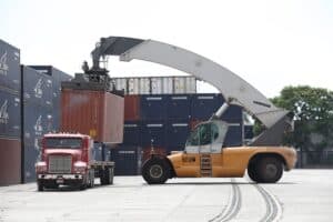 Contemporary cargo handling at a shipping yard with a forklift moving containers.