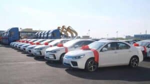 A fleet of new white sedans with red ribbons on the hood parked in a row at China Vast Logistics facility.