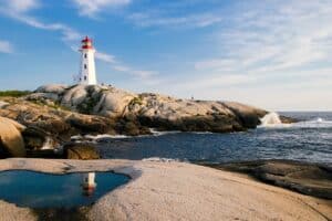 Lighthouse on rocky coastline with ocean waves under blue sky, representing maritime logistics and shipping in China.