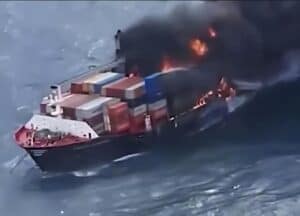 Container ship on fire at sea with stacked shipping containers burning and thick black smoke rising