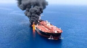 Oil tanker on fire in the middle of the ocean with thick black smoke rising and flames visible on deck