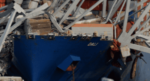 Bow of container ship "DALI" trapped under collapsed bridge structure with crushed shipping containers and twisted steel beams
