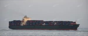 Container ship sailing at sea loaded with multiple rows of stacked shipping containers