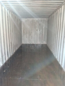 Empty interior of a standard shipping container, showing steel walls and wooden flooring