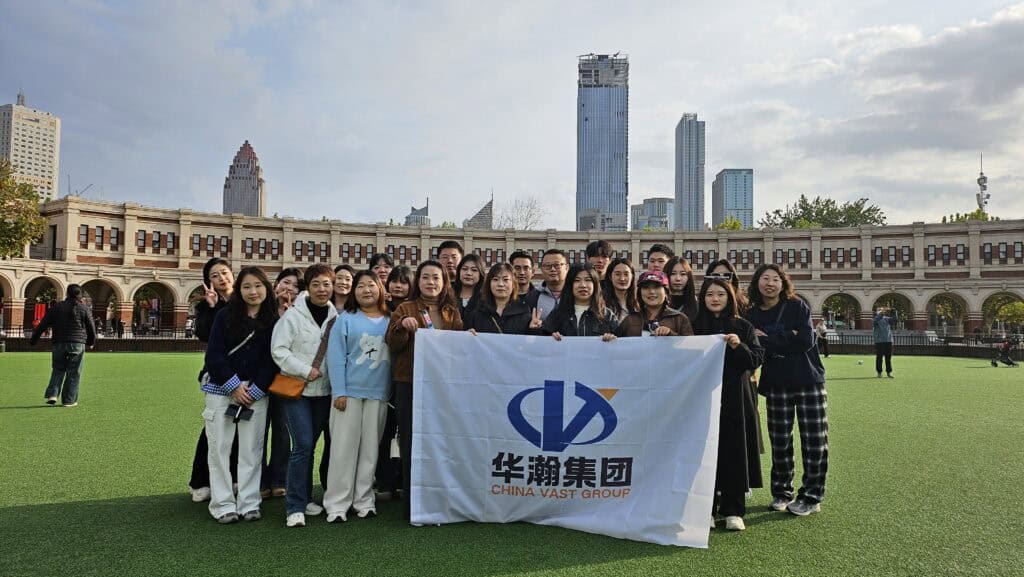 Group photo of China Vast Group employees holding company flag during autumn outing, with city skyline and green field in the background