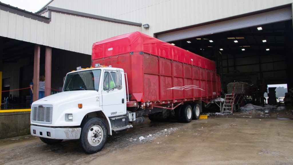 White truck with a red cargo body parked beside a warehouse loading area